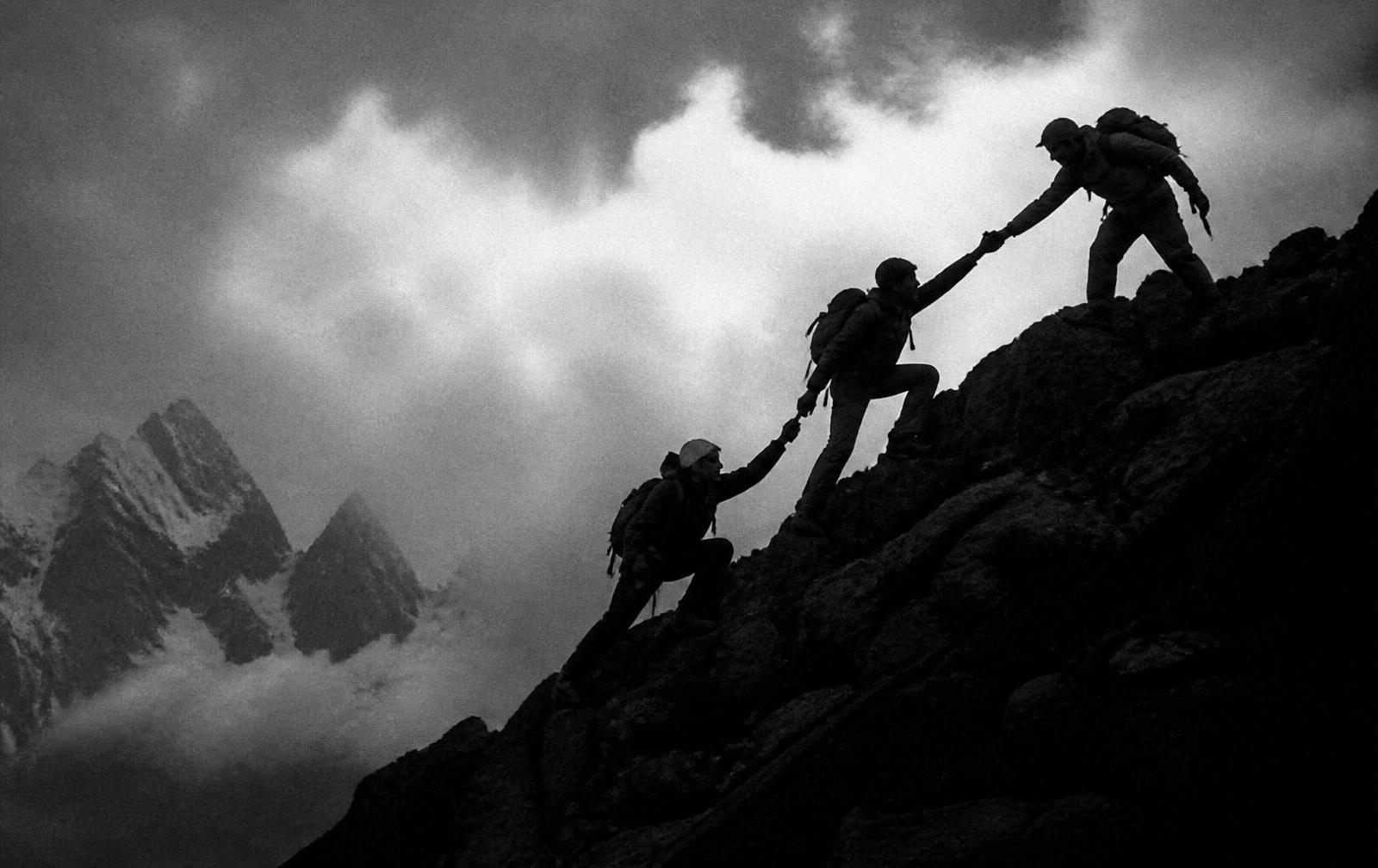 Climbers helping each other up a mountain ridge